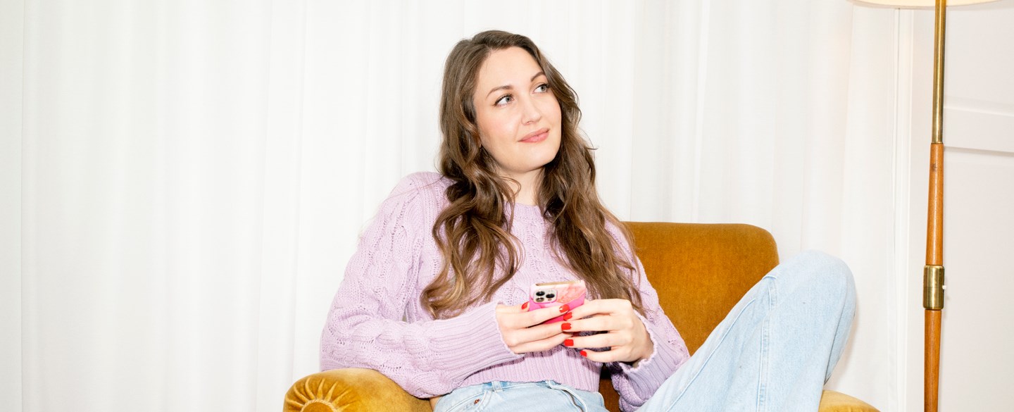 En kvinna sitter i en fåtölj och håller i en mobil.