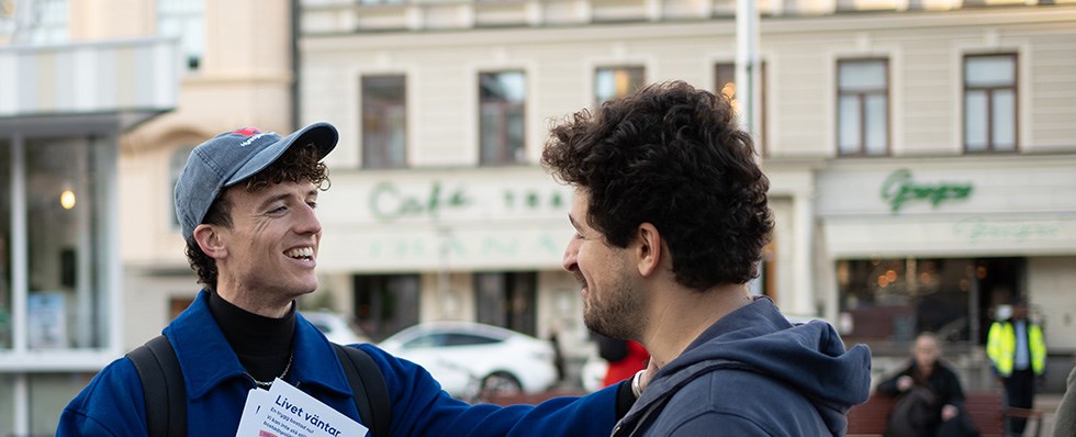 Foto på Ola Palmgren som står och pratar med en kille. I handen har han en flyer och på jackan sitter en pin med Hyresgästföreningens logga.