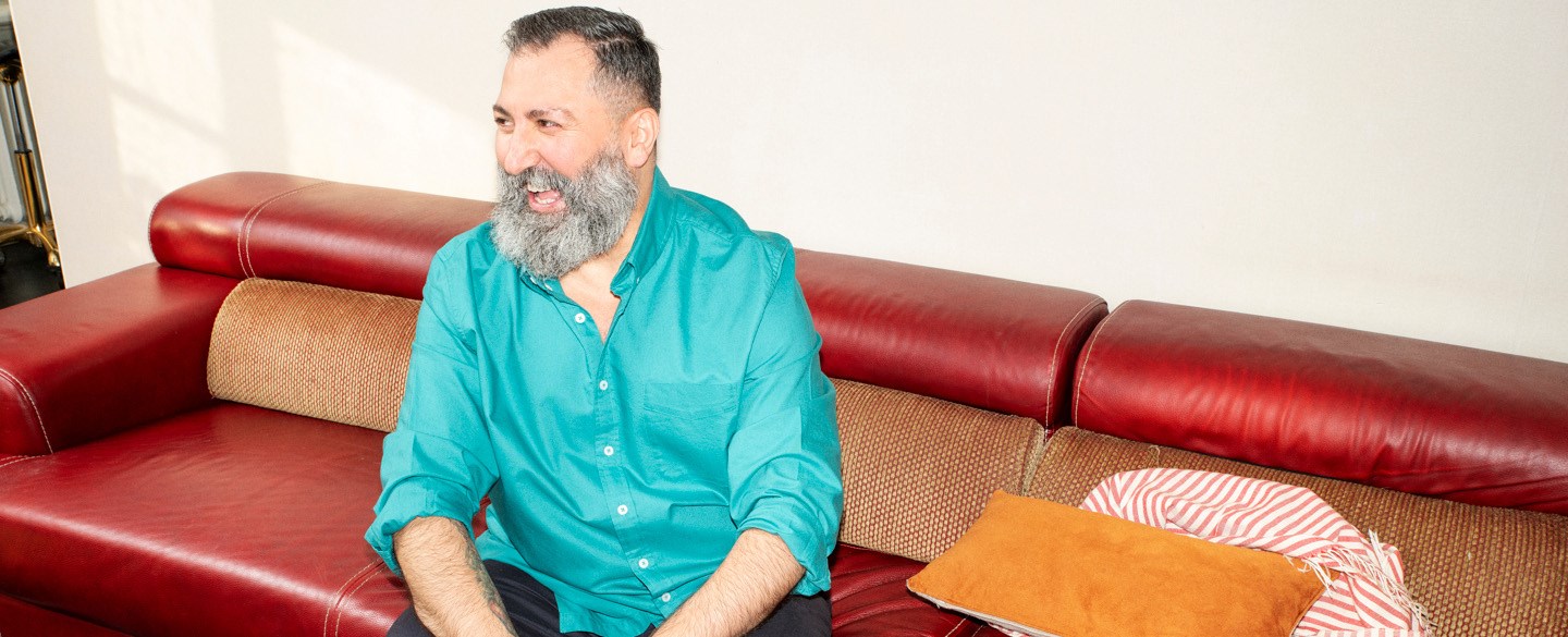 En man i blå skjorta sitter i en soffa.