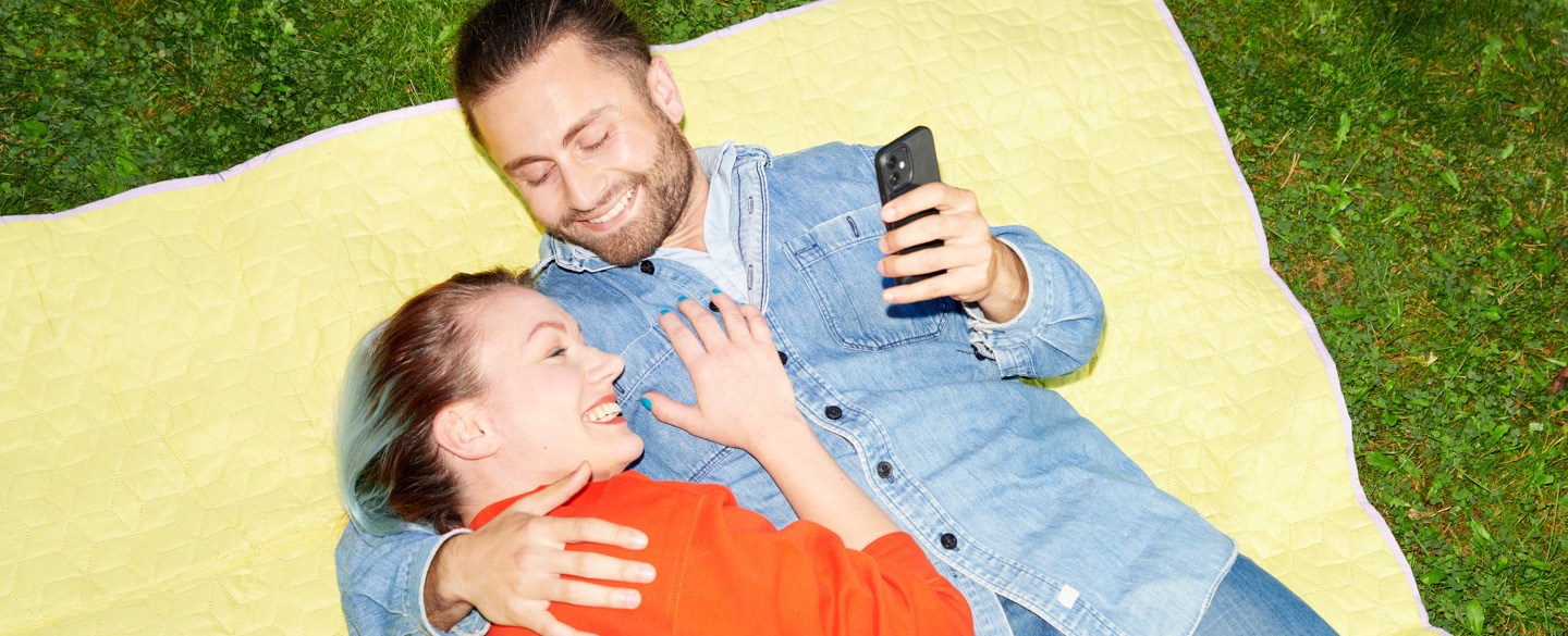 En man och en kvinna ligger på en filt på gräset och håller om varandra.