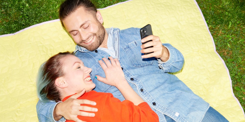 En man och en kvinna ligger på en filt på gräset och håller om varandra.