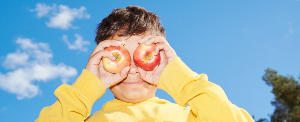 Blå himmel, pojke håller två äpplen framför ögonen