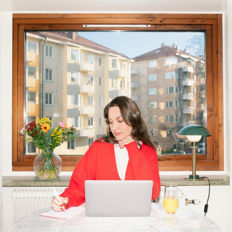 En kvinna sitter vid ett bord och antecknar något på ett papper.