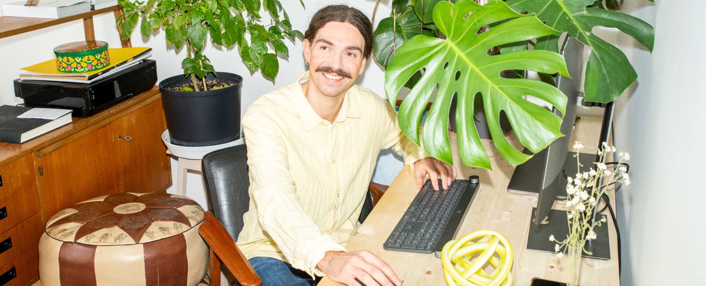 En ung man sitter vid sett skrivbord och arbetar.