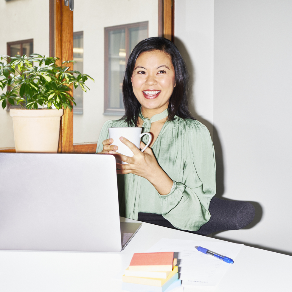 En kvinna sitter framför en dator och håller i en kaffekopp.