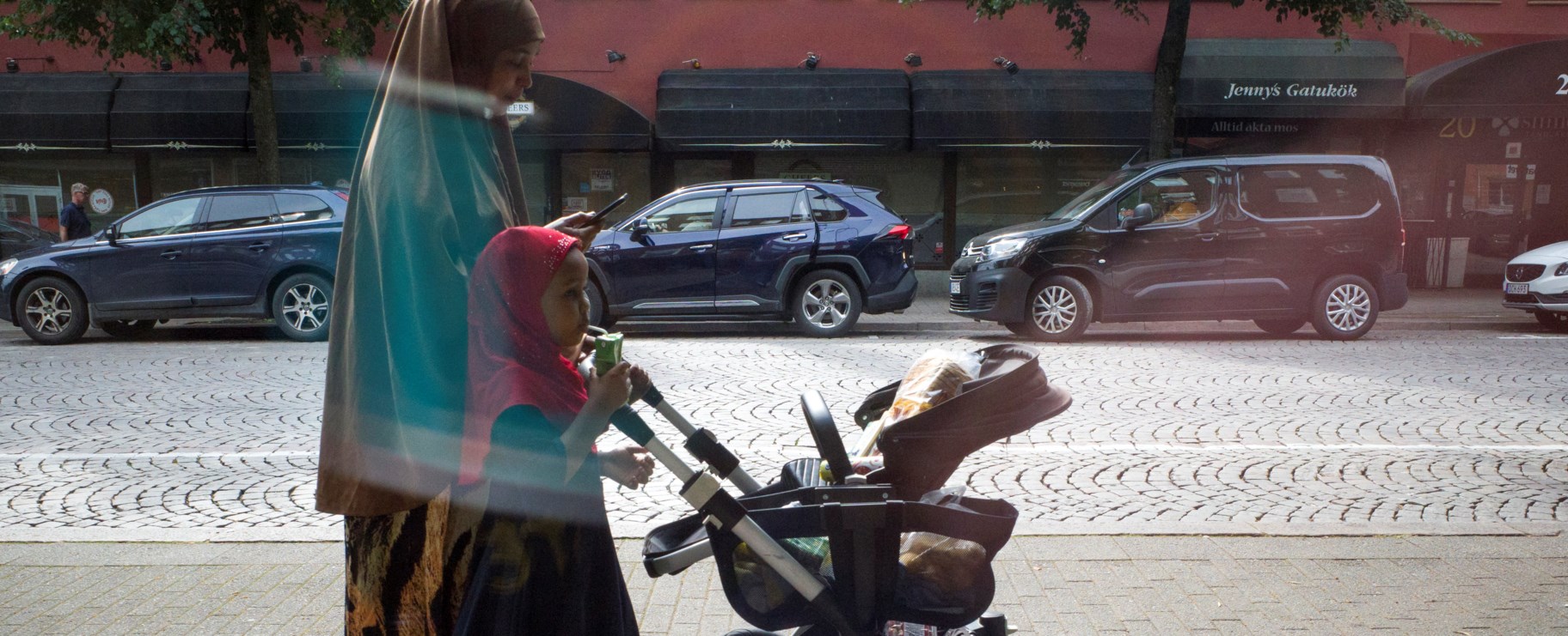 Barnvagn, mamma och  barn med slöja promenerar i Borås