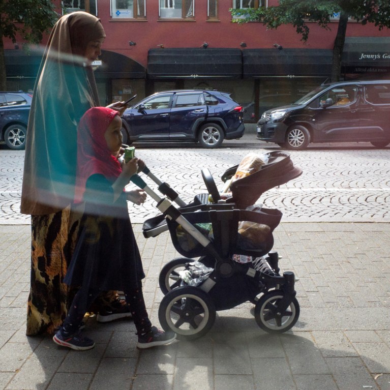 Barnvagn, mamma och  barn med slöja promenerar i Borås